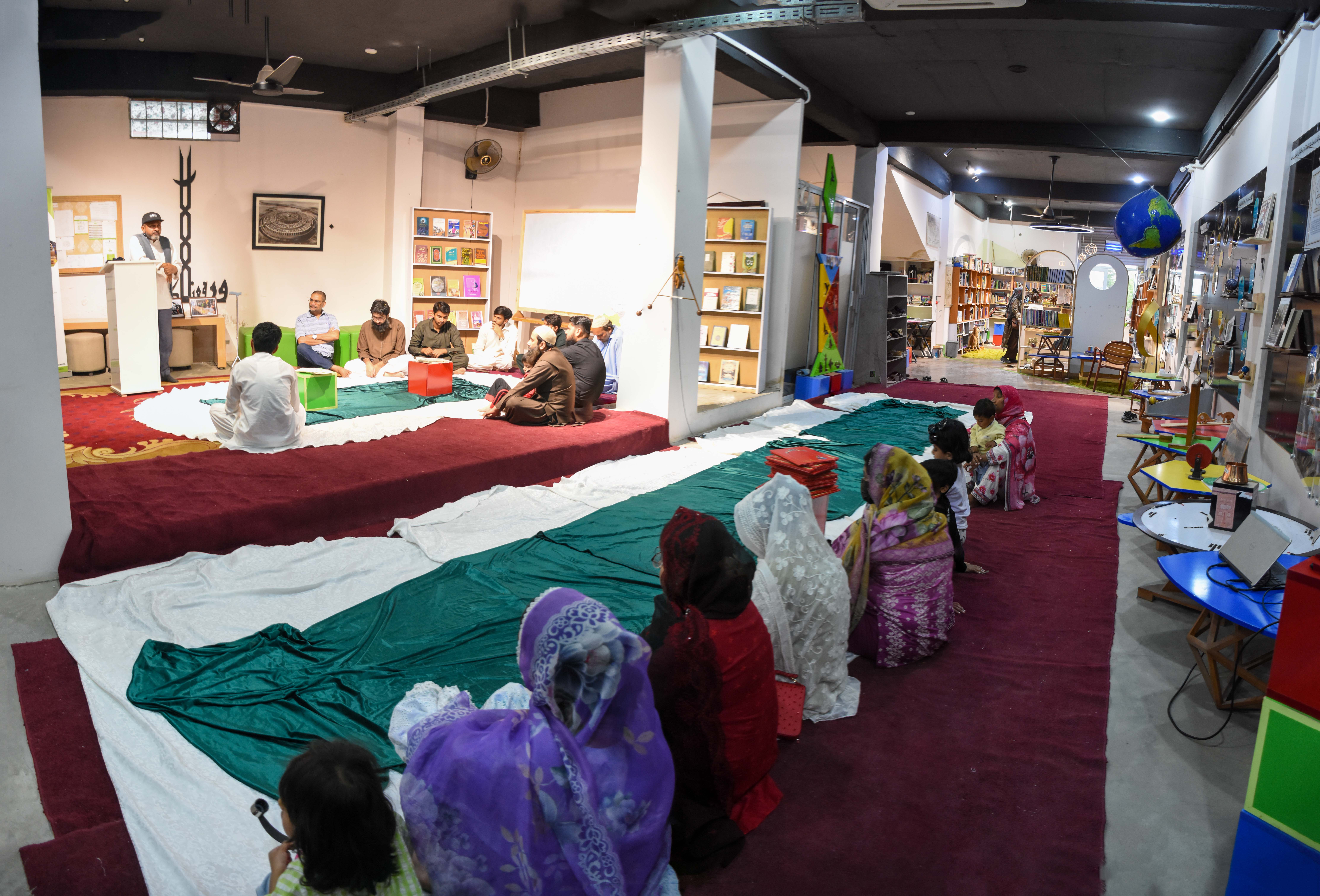 Unity — Women and girls in colorful headscarves stand together in neat rows at the back of the hall, uniting with the men in collective prayer.