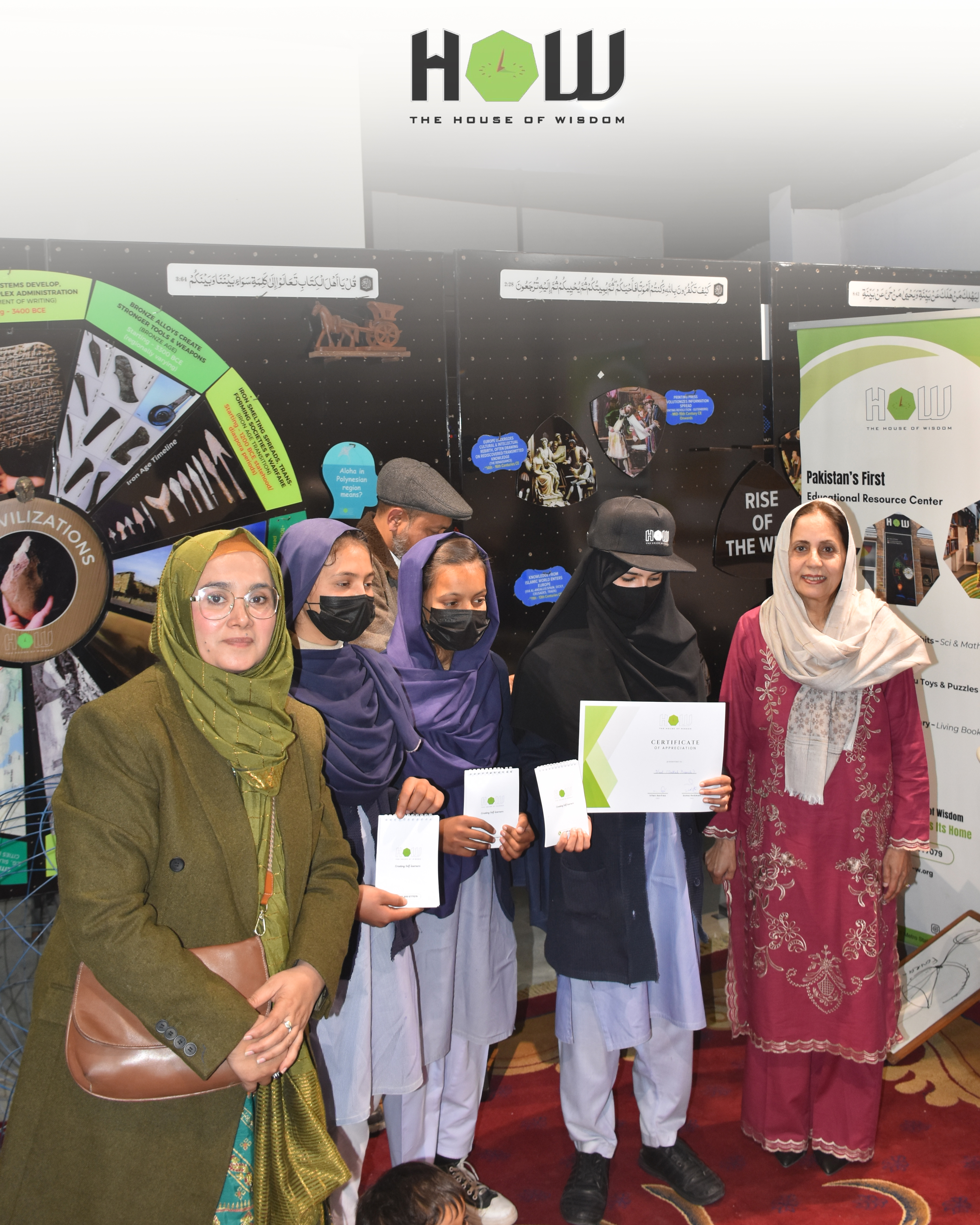 Achievement — girls holding certificates beside their tsunami project with a mentor